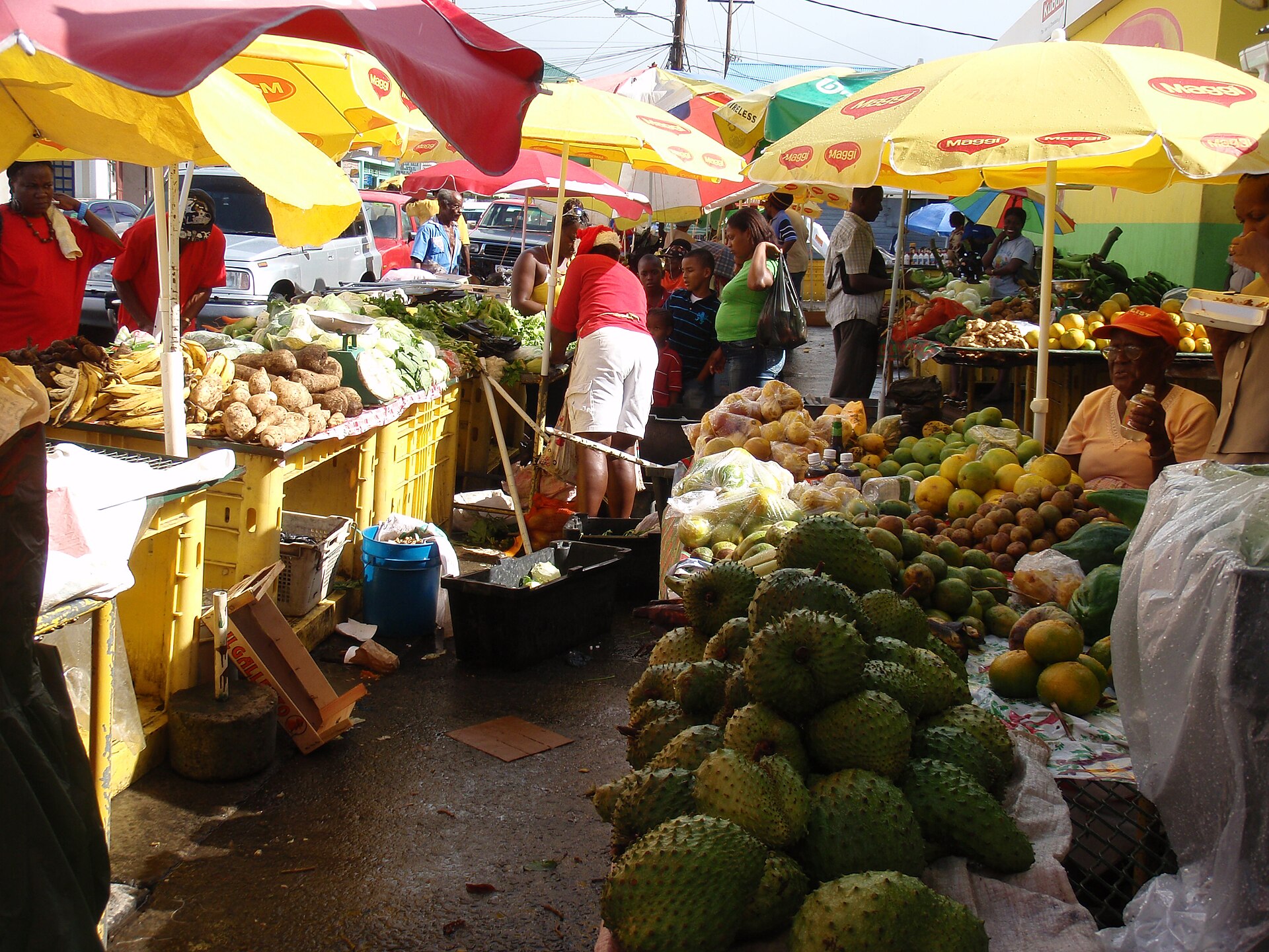 Roseau Saturday market stalls under yellow umbrellas, piled with soursop, mangoes and root crops