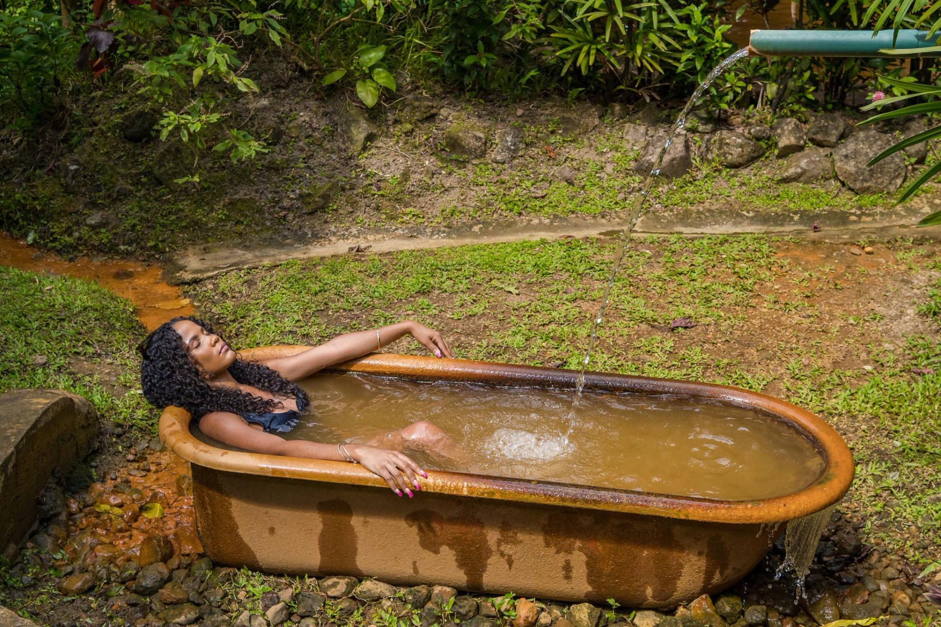 A traveller resting in a copper tub as spring water pours from a bamboo pipe