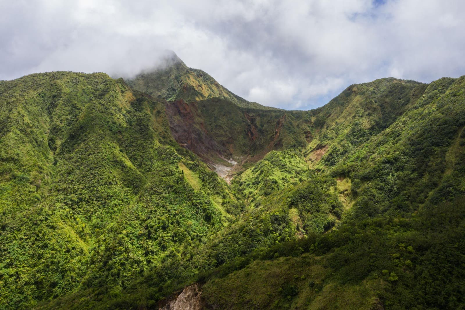 Green volcanic ridges with mineral-stained slopes rising to a cloud-wrapped peak in Dominica