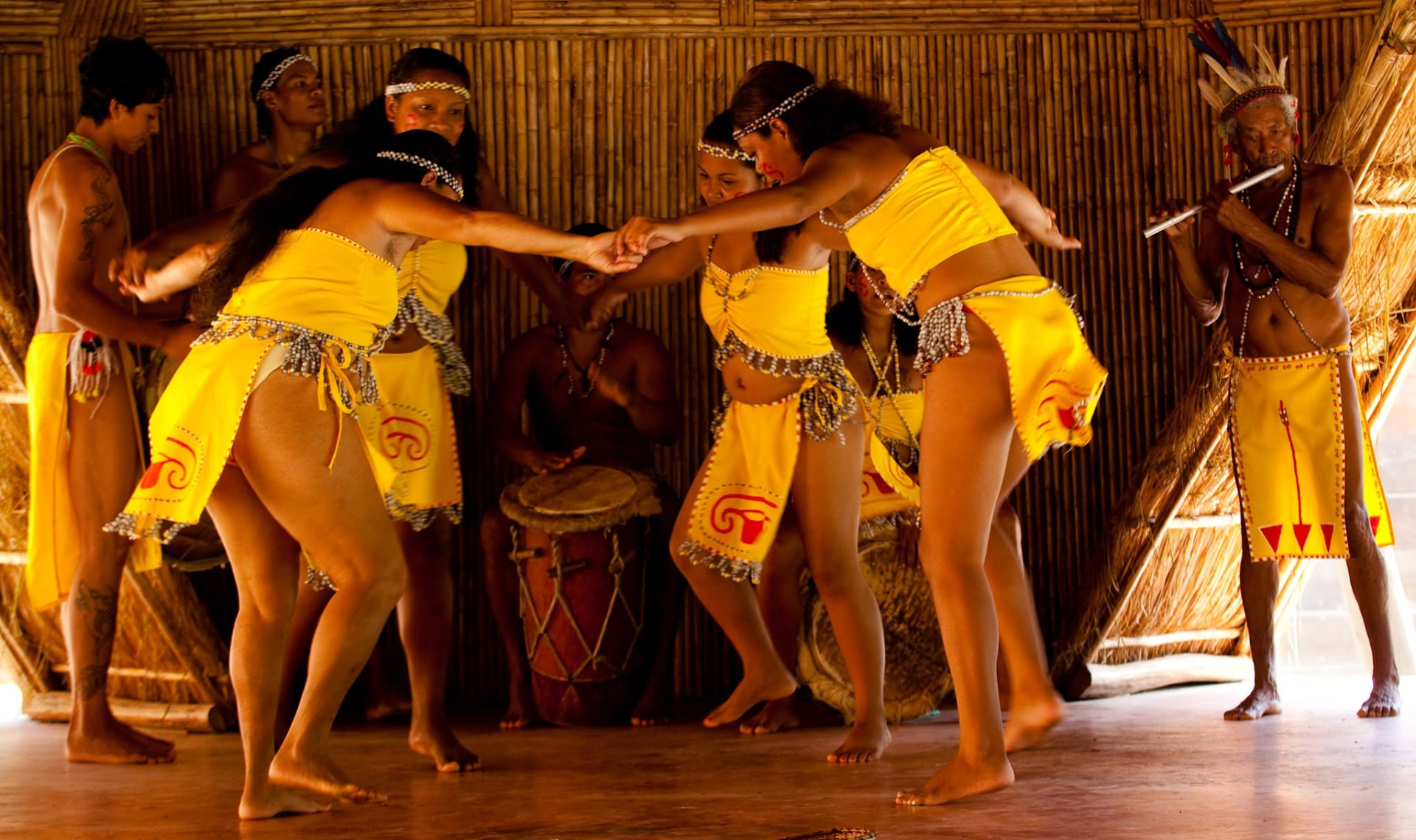 Kalinago dancers in traditional yellow dress inside a bamboo karbet
