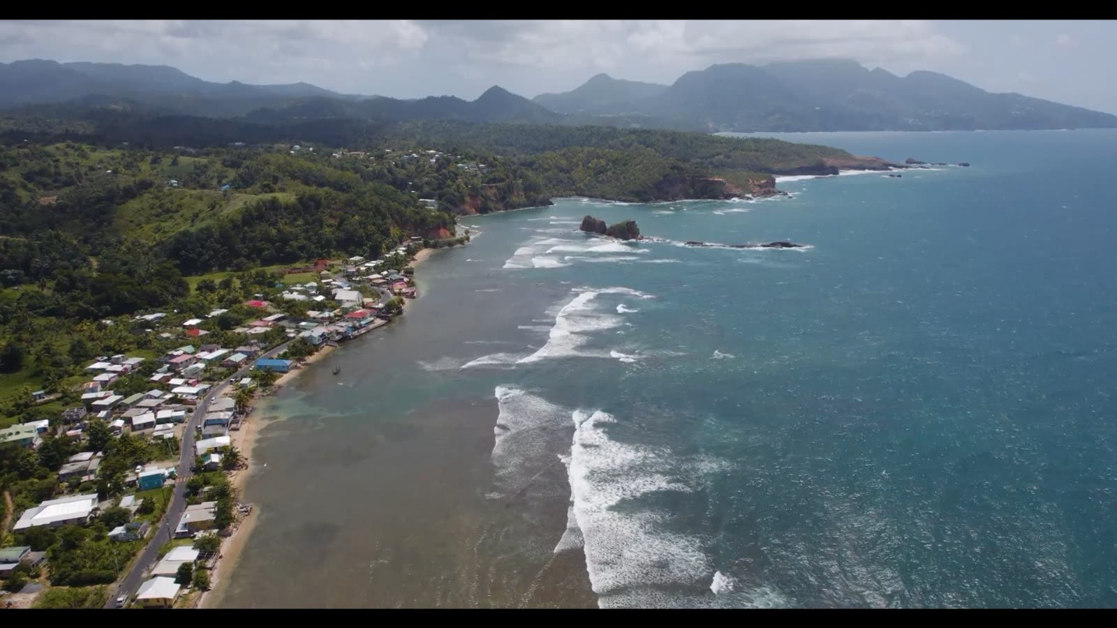 Aerial view of Atlantic surf rolling past a Kalinago coastal village