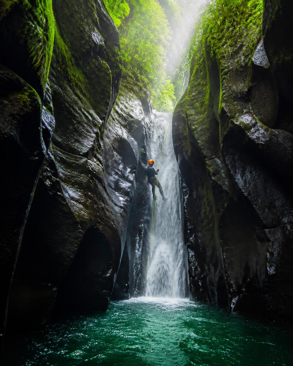 Canyoneer rappelling down a waterfall in a Dominica river gorge
